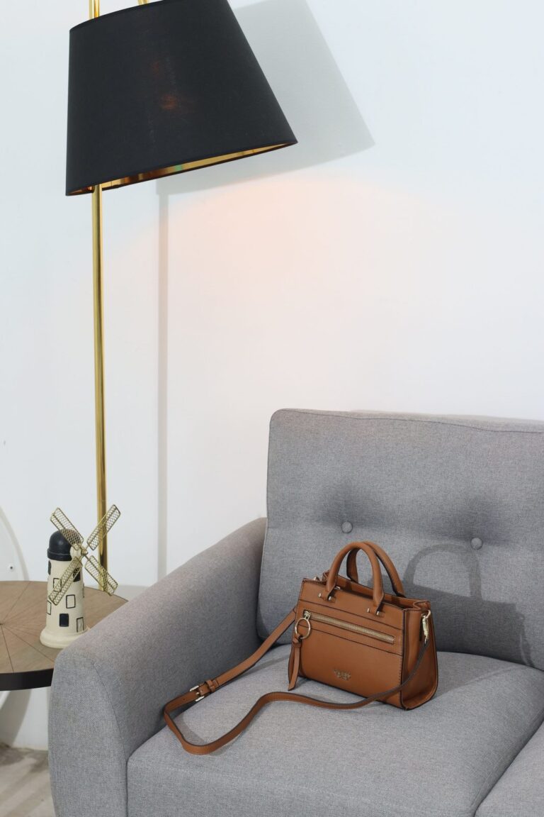 Bolso de piel en tono cuero sobre un sofá, iluminado por una lámpara (imagen de referencia de bolsos y complementos)