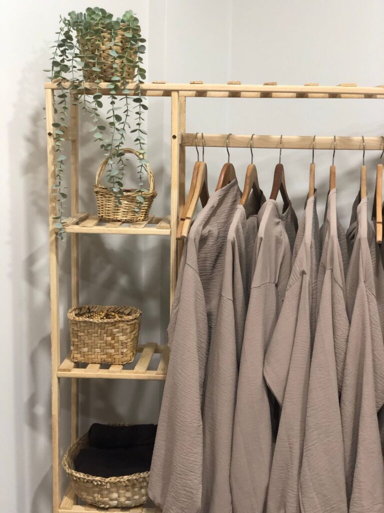 Prendas de lino colgadas en una percha de madera junto a cestas de mimbre (imagen de referencia de moda y textil)