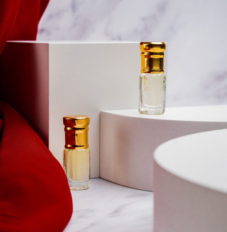 Dos frascos de perfume con tapón dorado sobre mármol y tela granate (imagen de referencia de perfumería)
