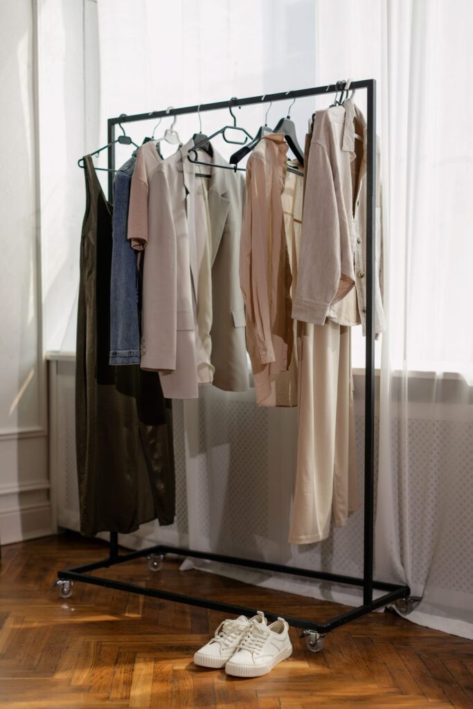 Percha con prendas de ropa en tonos neutros junto a una ventana (imagen de referencia de la categoría de moda)