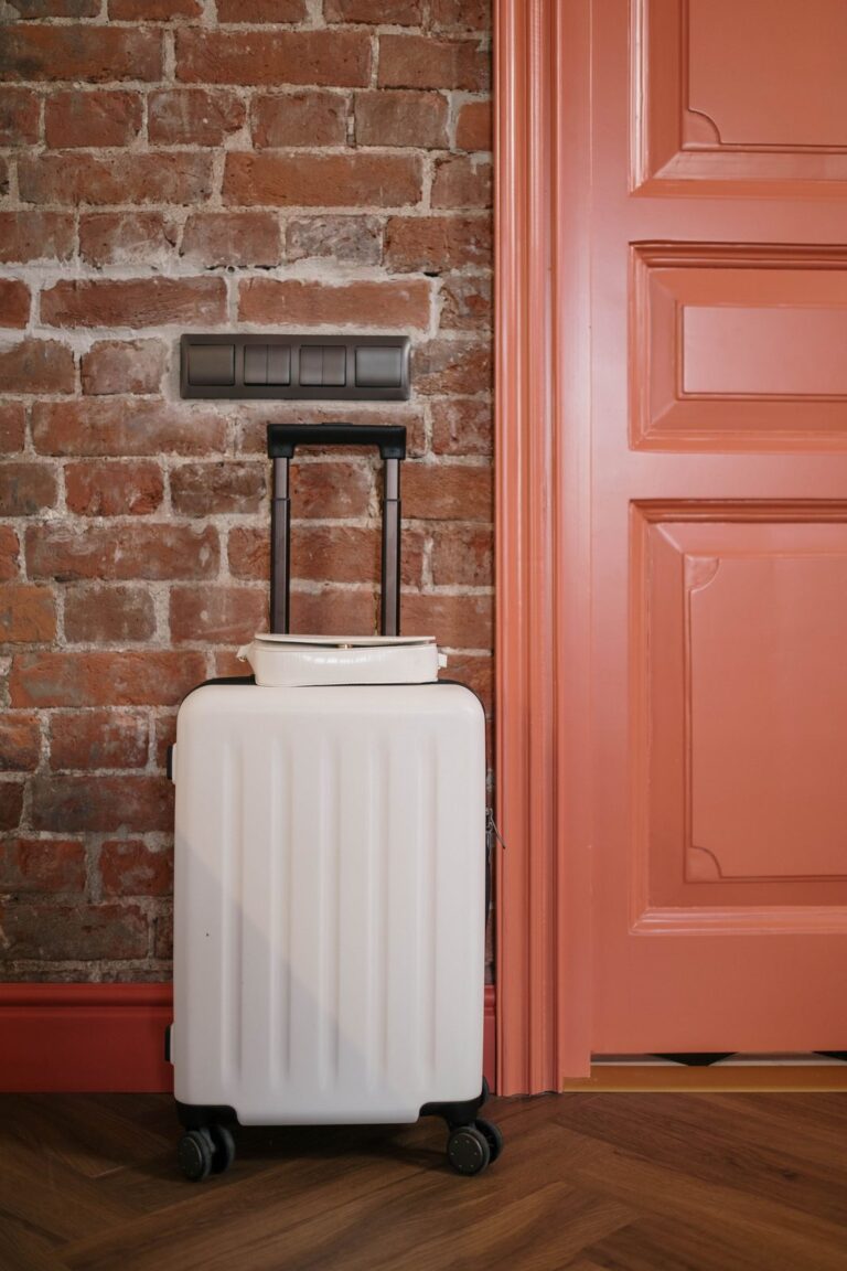 Maleta de mano de color crema con un bolso encima junto a la puerta de una vivienda (imagen de referencia de maletas y viaje)